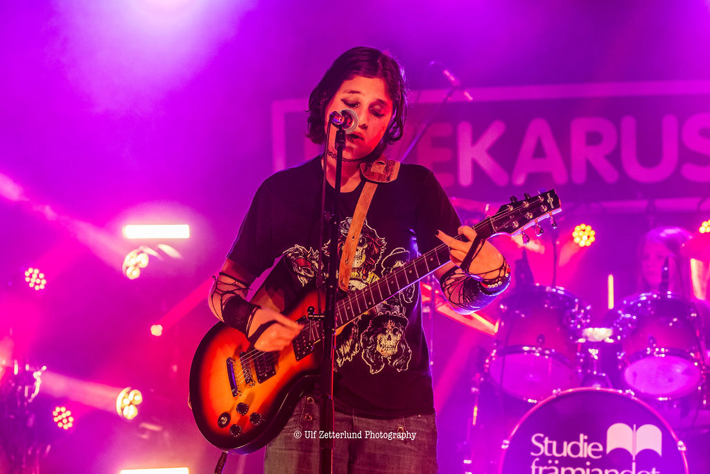 En gitarrist på en scen som badar i lila ljus.