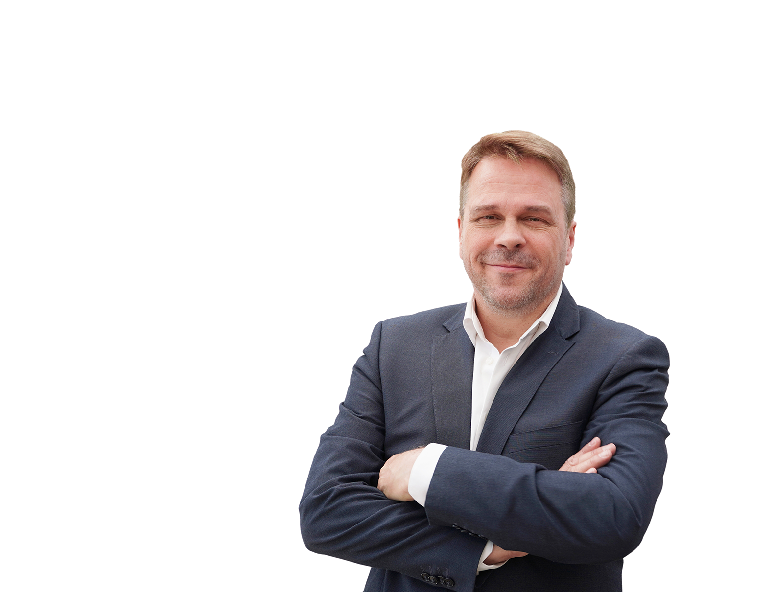 En man klädd i kostym står med händerna i kors och ler.