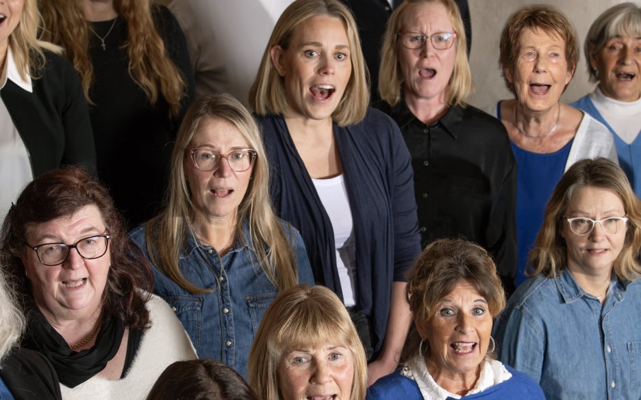 Kör med kvinnor klädda i blått och vitt sjunger.